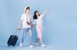 A happy couple with a suitcase, walking together and pointing forward while traveling.